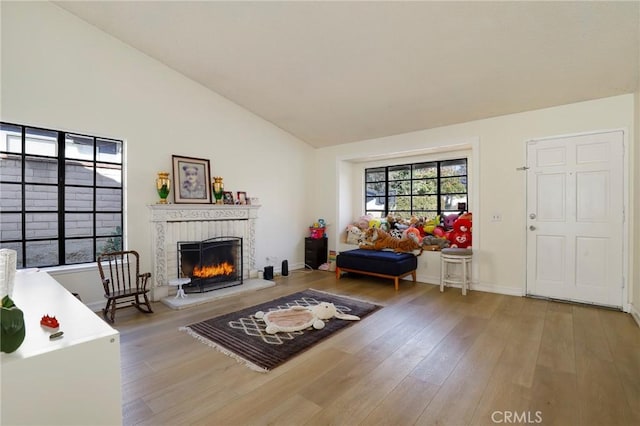 living room featuring a healthy amount of sunlight, lofted ceiling, hardwood / wood-style floors, and a brick fireplace