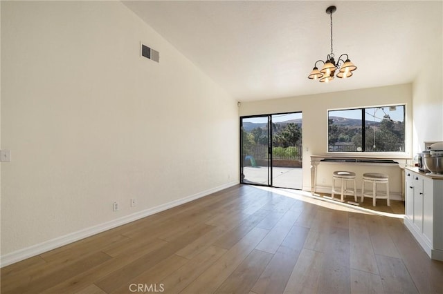 interior space with an inviting chandelier, vaulted ceiling, and hardwood / wood-style flooring