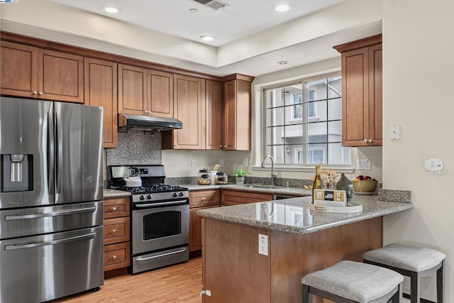 kitchen with sink, a breakfast bar, appliances with stainless steel finishes, light stone counters, and kitchen peninsula