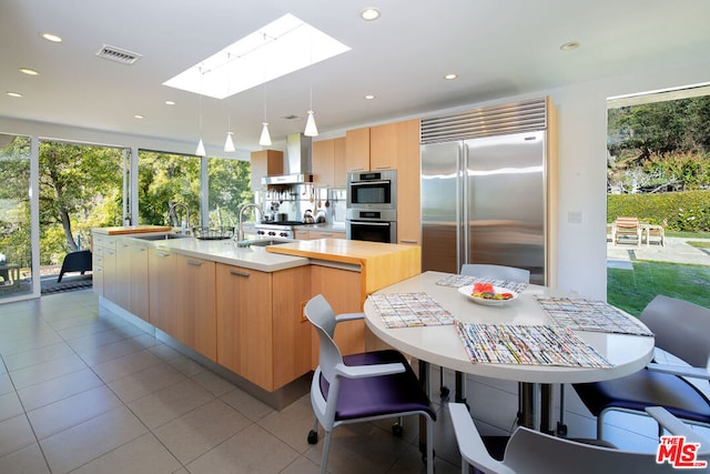 kitchen featuring a kitchen island with sink, exhaust hood, hanging light fixtures, a skylight, and appliances with stainless steel finishes