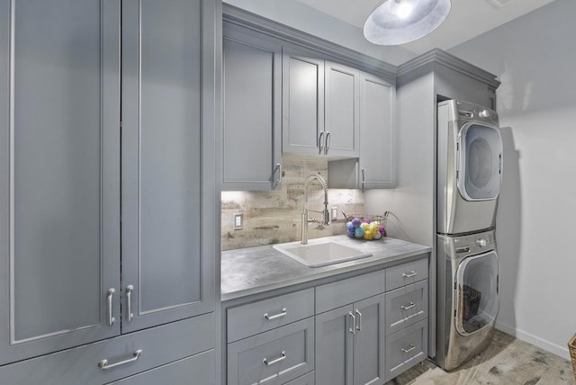 clothes washing area featuring cabinets, sink, stacked washing maching and dryer, and light hardwood / wood-style floors