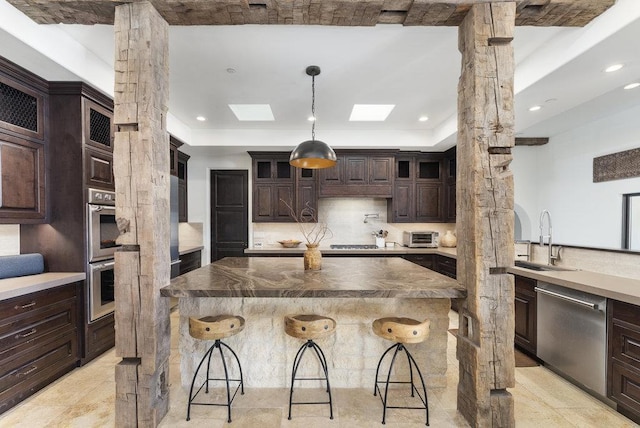 kitchen featuring a kitchen bar, sink, dark brown cabinetry, a skylight, and stainless steel appliances