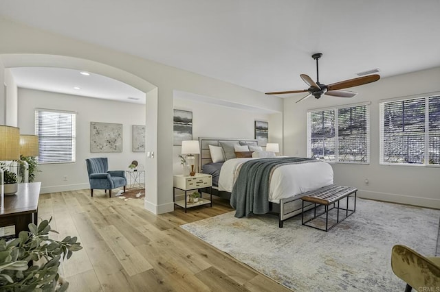 bedroom with visible vents, baseboards, wood finished floors, arched walkways, and a ceiling fan