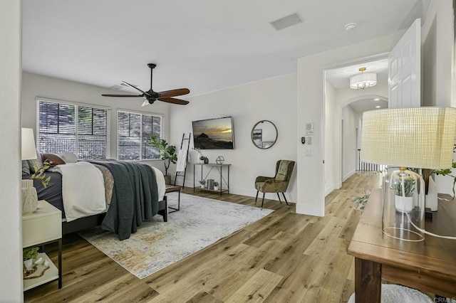 bedroom with light wood finished floors, arched walkways, baseboards, and ceiling fan