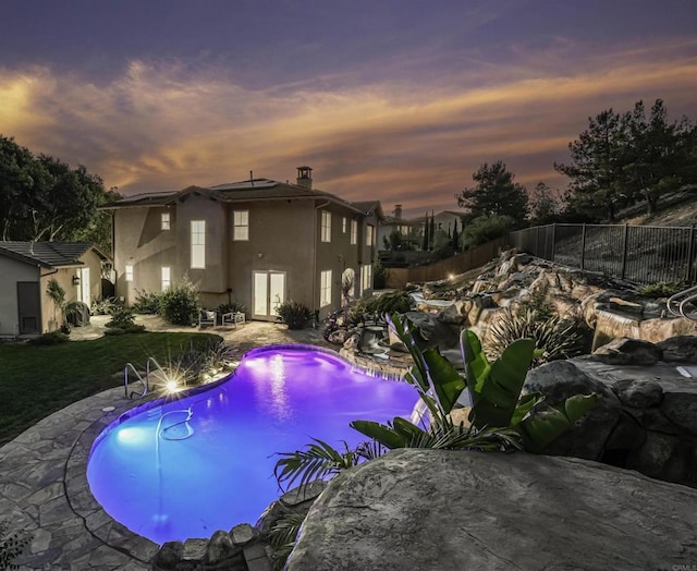 pool at dusk featuring a fenced in pool, a lawn, a fenced backyard, a patio area, and an outbuilding