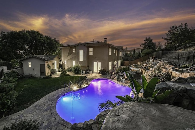 pool at dusk with a fenced in pool, a yard, a fenced backyard, a patio area, and an outbuilding