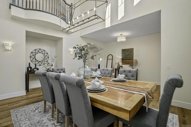 dining space with a high ceiling, wood finished floors, arched walkways, and baseboards