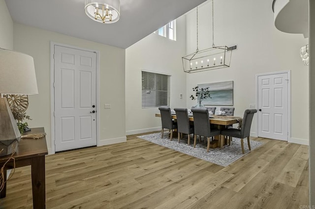 dining space featuring baseboards, light wood-type flooring, a towering ceiling, and a chandelier