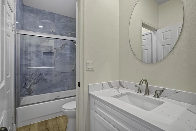 full bathroom with toilet, wood finished floors, combined bath / shower with glass door, vanity, and a textured wall