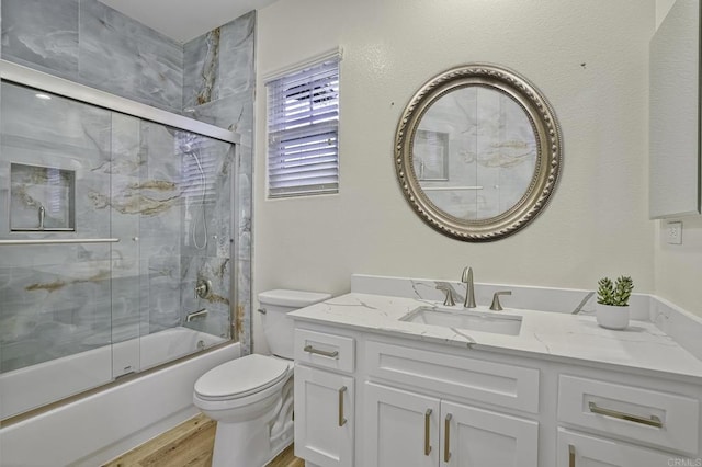 bathroom with vanity, toilet, wood finished floors, and enclosed tub / shower combo