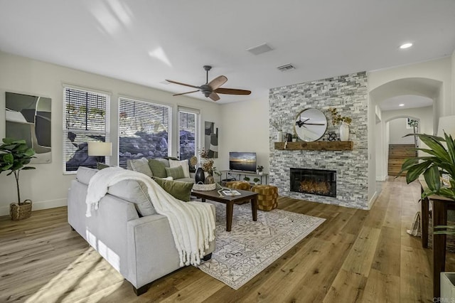 living room featuring visible vents, ceiling fan, a stone fireplace, wood finished floors, and arched walkways