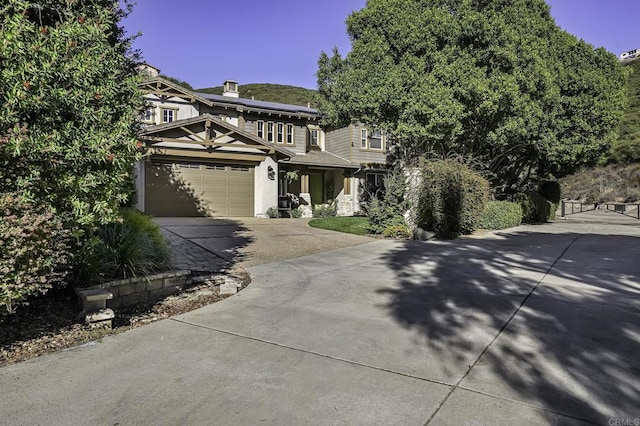 view of property hidden behind natural elements with a chimney, solar panels, and driveway