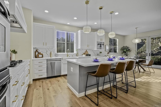 kitchen with light wood finished floors, a center island, a breakfast bar, appliances with stainless steel finishes, and white cabinets