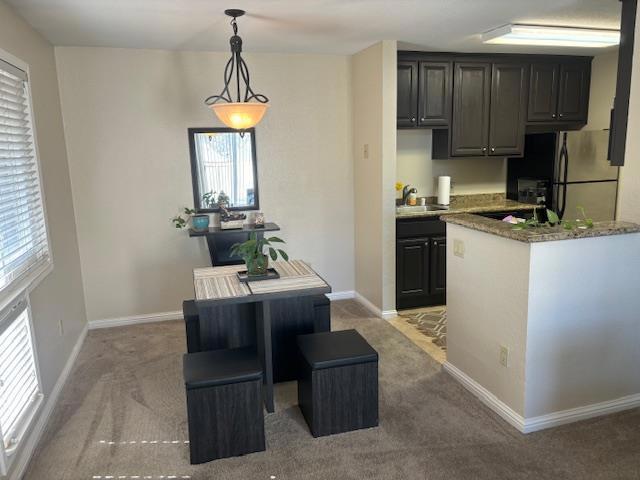 kitchen with a kitchen island, stainless steel refrigerator, hanging light fixtures, light carpet, and light stone counters