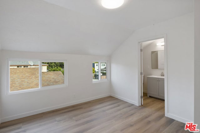 unfurnished bedroom with light hardwood / wood-style flooring, vaulted ceiling, ensuite bath, and sink