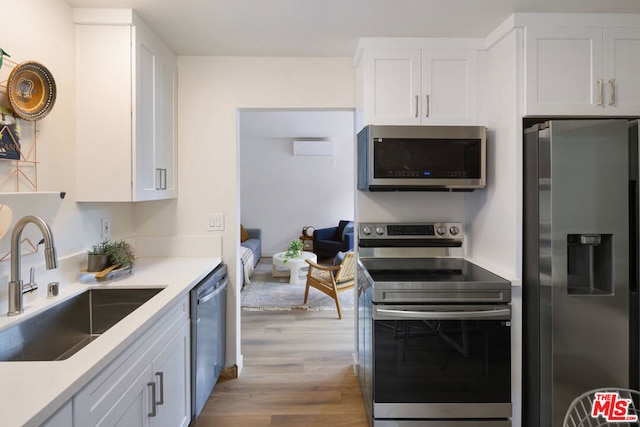 kitchen with white cabinetry, sink, a wall unit AC, appliances with stainless steel finishes, and light wood-type flooring