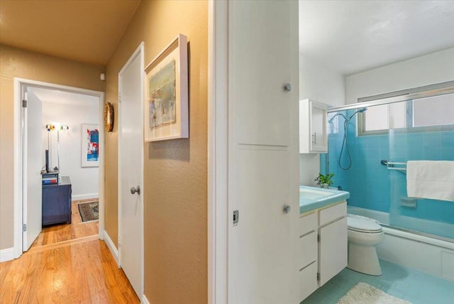 full bathroom with wood-type flooring, combined bath / shower with glass door, toilet, and vanity