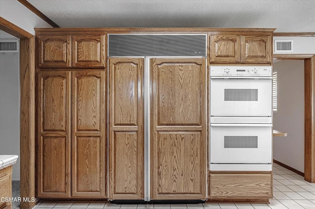 kitchen featuring a textured ceiling, paneled built in fridge, light tile patterned floors, double oven, and ornamental molding