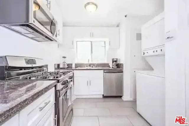 kitchen featuring dark stone counters, white cabinets, sink, light tile patterned floors, and stainless steel appliances