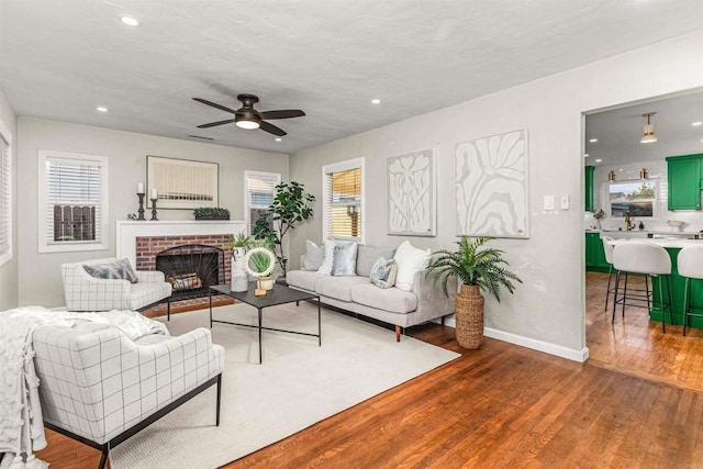 living room with ceiling fan, hardwood / wood-style floors, a wealth of natural light, and a brick fireplace