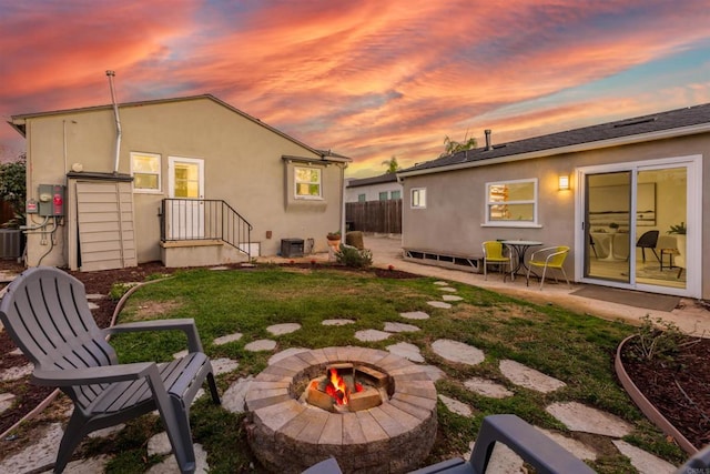 back house at dusk with an outdoor fire pit, a patio area, a lawn, and central AC unit