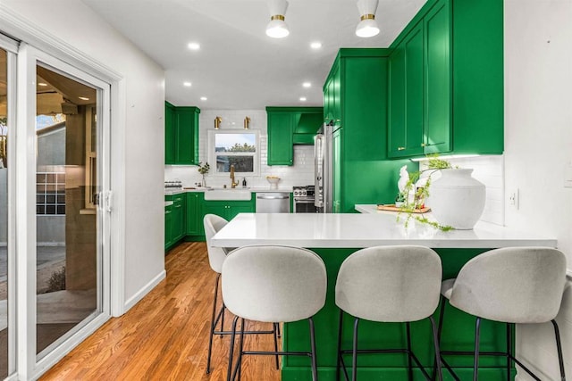 kitchen with stainless steel appliances, kitchen peninsula, sink, light hardwood / wood-style flooring, and backsplash