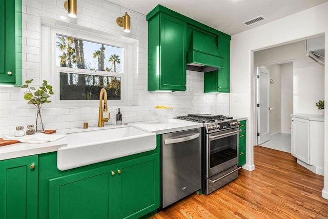 kitchen with stainless steel appliances, green cabinetry, custom range hood, decorative backsplash, and sink