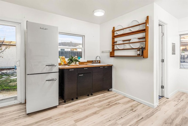 bar with white fridge, light hardwood / wood-style flooring, dark brown cabinets, and sink