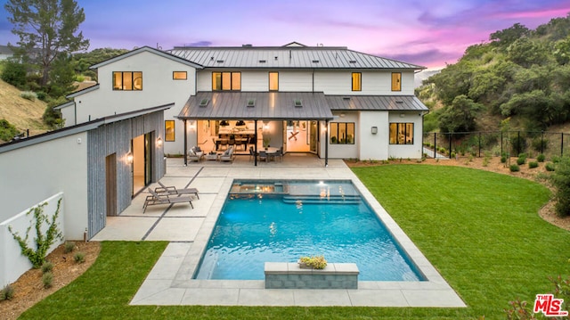 back house at dusk featuring a lawn, a patio area, and a fenced in pool