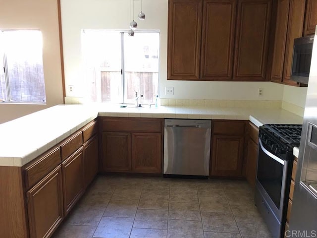 kitchen with pendant lighting, sink, tile counters, kitchen peninsula, and stainless steel appliances