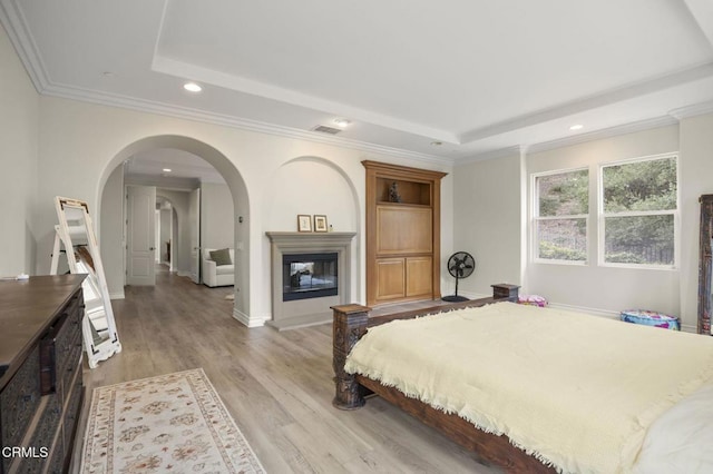 bedroom featuring a tray ceiling, light hardwood / wood-style flooring, ornamental molding, and a large fireplace