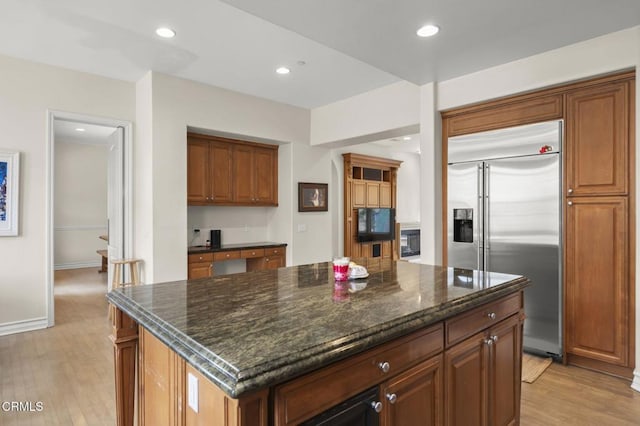 kitchen featuring light hardwood / wood-style flooring, a center island, built in appliances, and dark stone counters