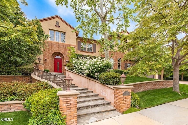 mediterranean / spanish home with a front yard, stucco siding, brick siding, and stairs