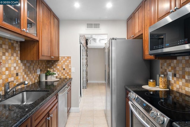 kitchen with sink, stainless steel appliances, backsplash, dark stone counters, and light tile patterned flooring