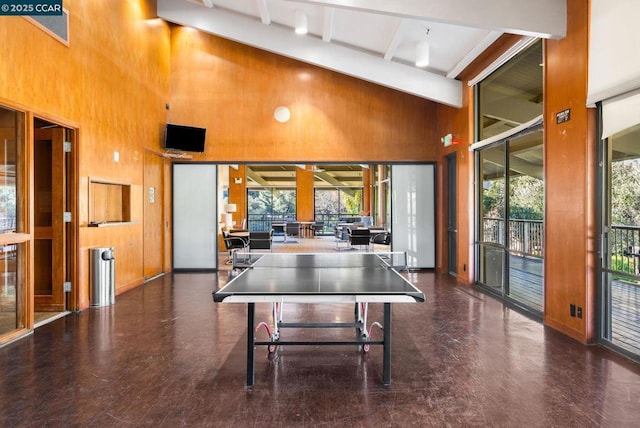 rec room featuring beamed ceiling, a towering ceiling, and wooden walls