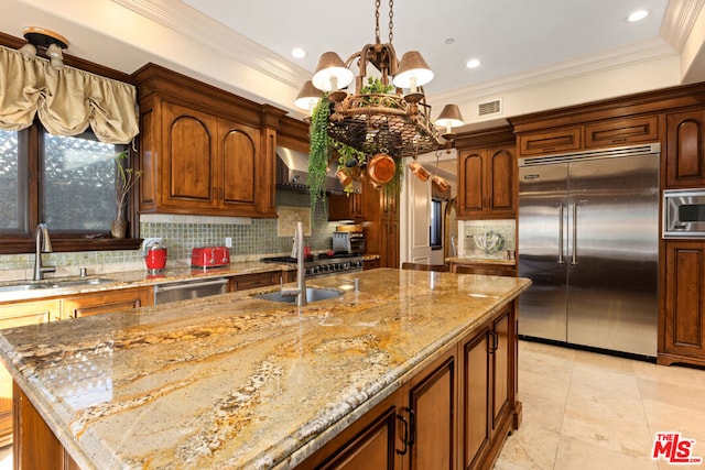 kitchen featuring wall chimney range hood, sink, built in appliances, a center island with sink, and an inviting chandelier