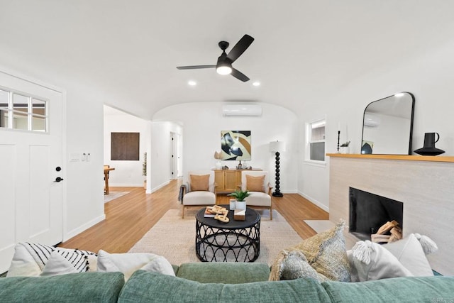 living room featuring light wood-type flooring, a wall mounted AC, and ceiling fan