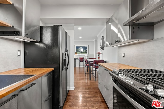 kitchen with stainless steel appliances, wood counters, dark hardwood / wood-style flooring, white cabinets, and wall chimney range hood