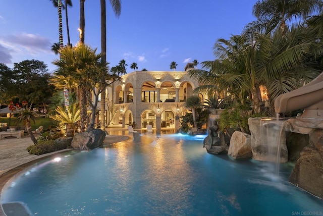 pool at dusk with pool water feature and a water slide