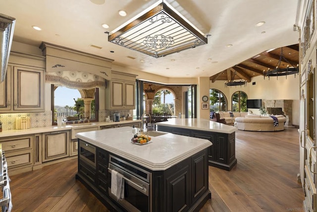 kitchen featuring sink, cream cabinets, an island with sink, decorative backsplash, and wood ceiling