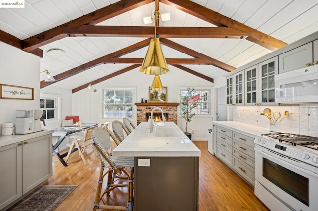 kitchen featuring gray cabinets, a kitchen island with sink, white appliances, and lofted ceiling with beams