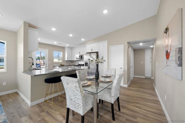 dining space featuring light hardwood / wood-style floors, lofted ceiling, and sink