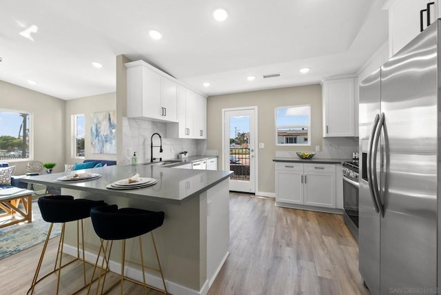 kitchen featuring kitchen peninsula, appliances with stainless steel finishes, sink, white cabinets, and light hardwood / wood-style floors