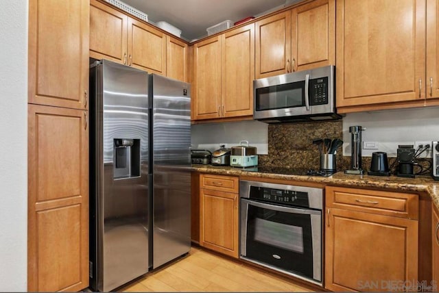 kitchen with decorative backsplash, appliances with stainless steel finishes, light hardwood / wood-style floors, and dark stone countertops