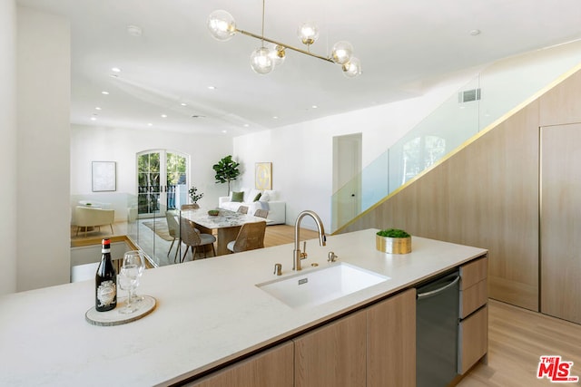 kitchen with light stone countertops, dishwasher, sink, hanging light fixtures, and light hardwood / wood-style floors