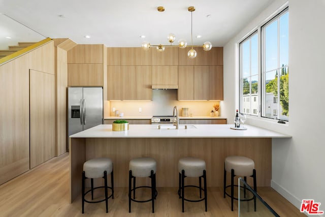 kitchen featuring a kitchen bar, stainless steel refrigerator with ice dispenser, sink, light hardwood / wood-style flooring, and hanging light fixtures