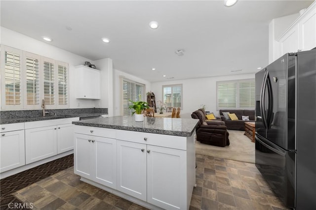 kitchen with sink, white cabinets, black fridge, and a center island