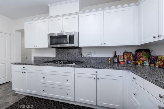 kitchen with tasteful backsplash, appliances with stainless steel finishes, dark stone countertops, and white cabinetry