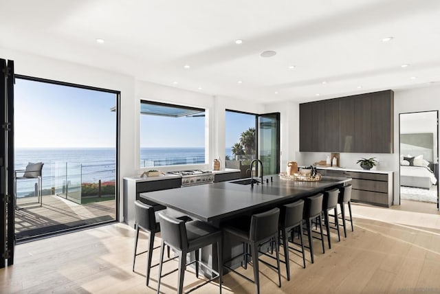 kitchen featuring a water view, sink, light wood-type flooring, dark brown cabinets, and a breakfast bar area