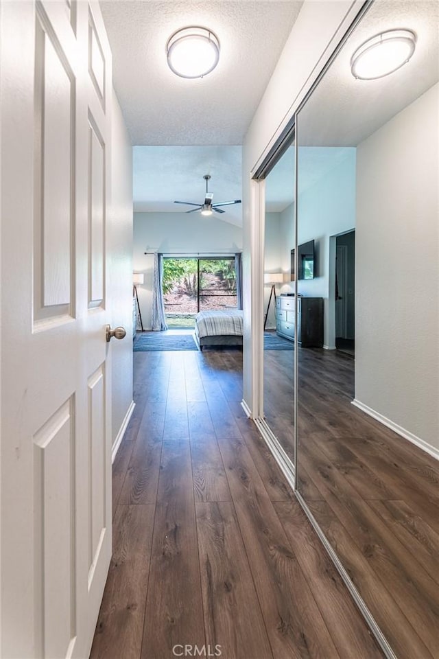 corridor with lofted ceiling, a textured ceiling, and dark wood-type flooring